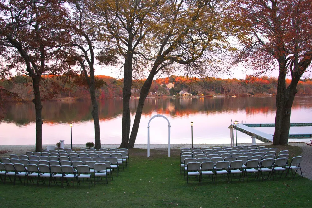 Ceremony chairs set on the lawn at the water’s edge at sunset